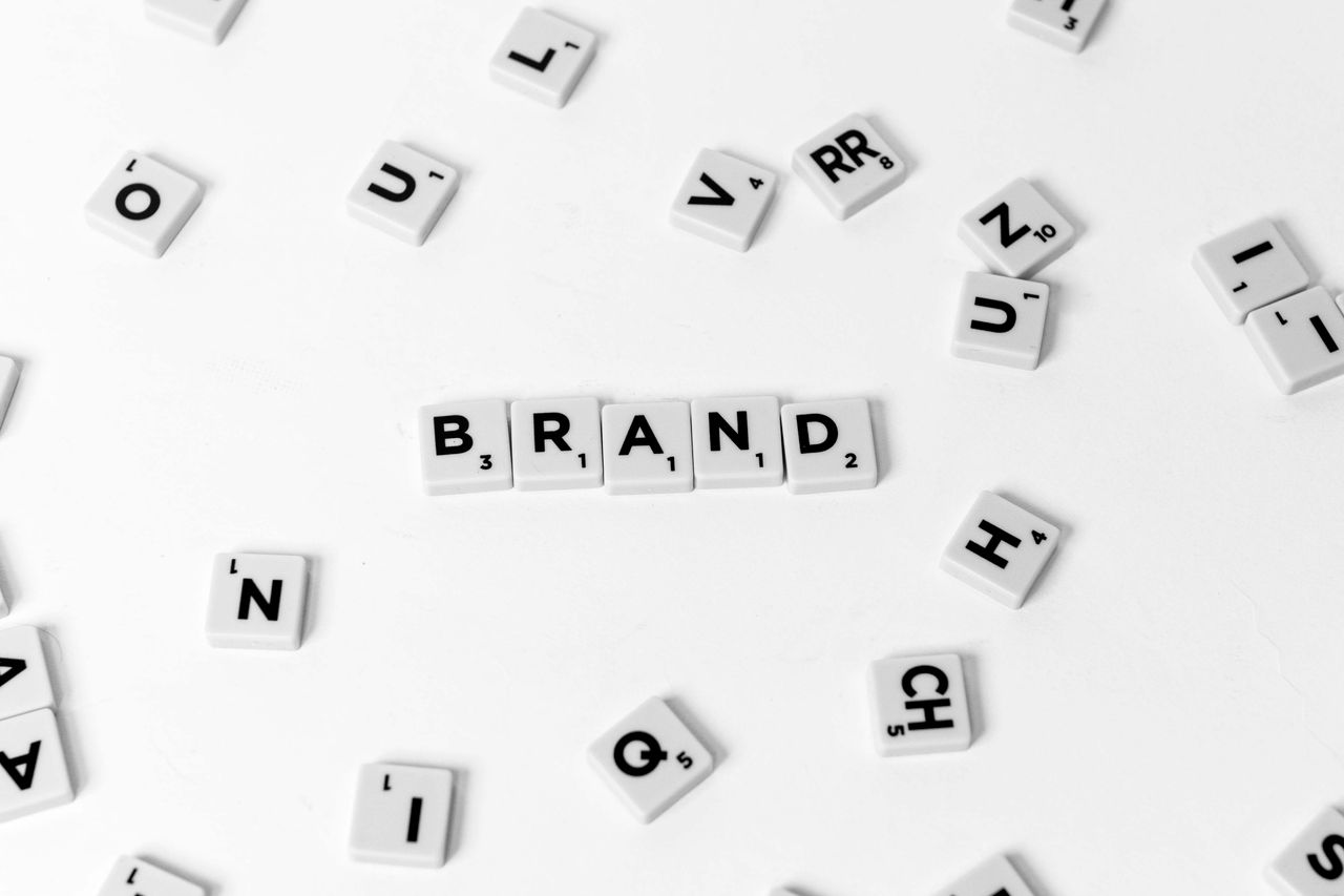 A flat lay of scattered letter tiles forming the word BRAND on a white background.